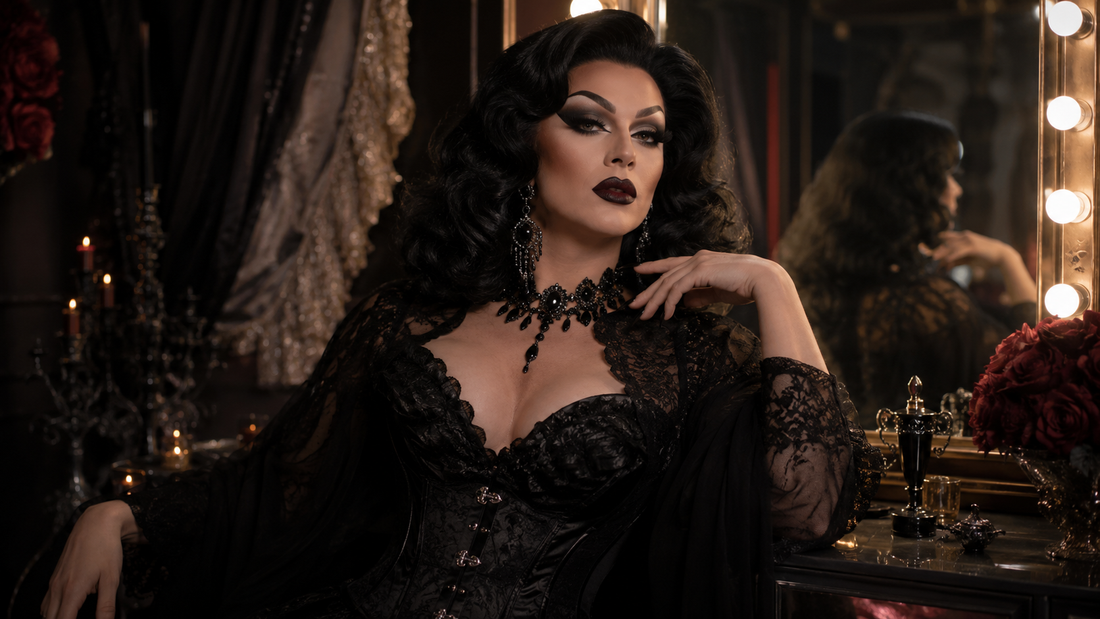 Drag queen avec look dark glam, maquillage intense, perruque volumineuse, tenue noire brillante et bijoux imposants dans une loge de spectacle.