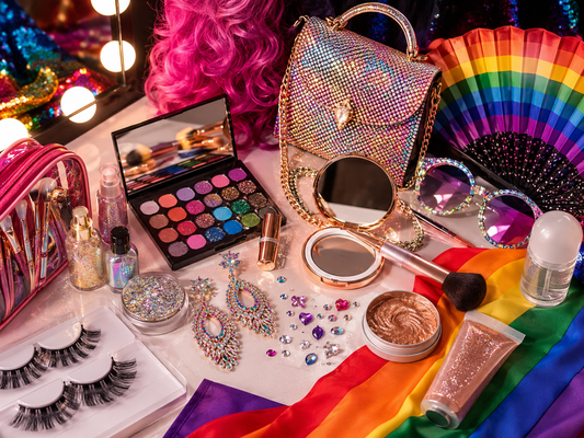 Drag queen préparant son kit Pride avec maquillage, perruque, talons, accessoires brillants et vêtements de scène dans une loge.