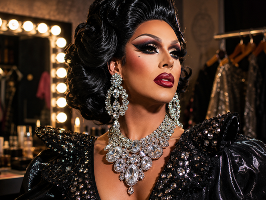 Drag queen devant un miroir de loge avec bijoux brillants, boucles d’oreilles, colliers et accessoires de scène.