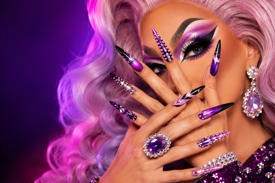 Drag queen avec maquillage glamour et longs faux ongles posant dans une loge éclairée par des lumières de miroir.